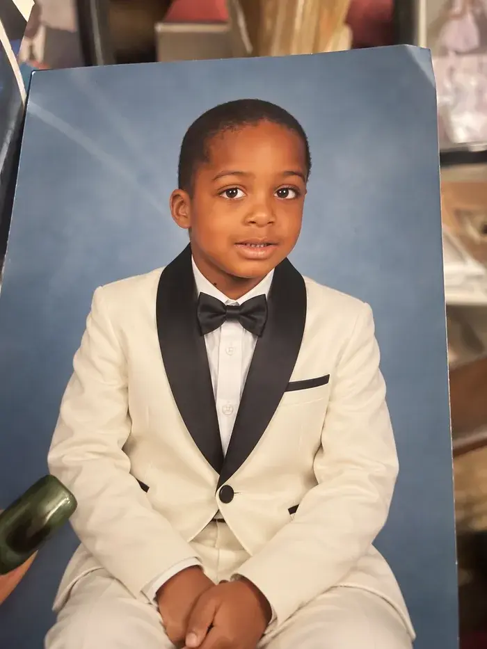 After: the same portrait edited to an ivory tuxedo with a black bow tie, pose and blue background preserved exactly